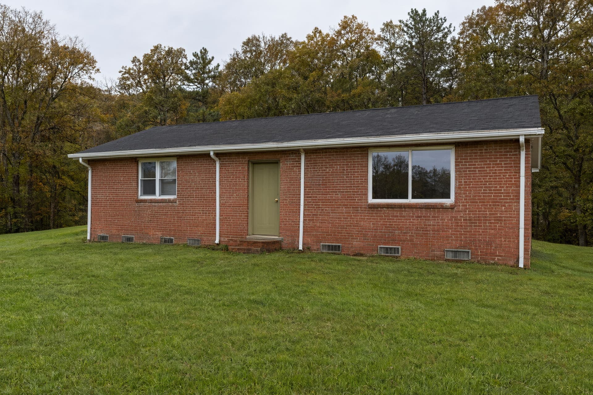 Single-story red brick ranch house with foundation vents along the base and white gutters on a gentle slope